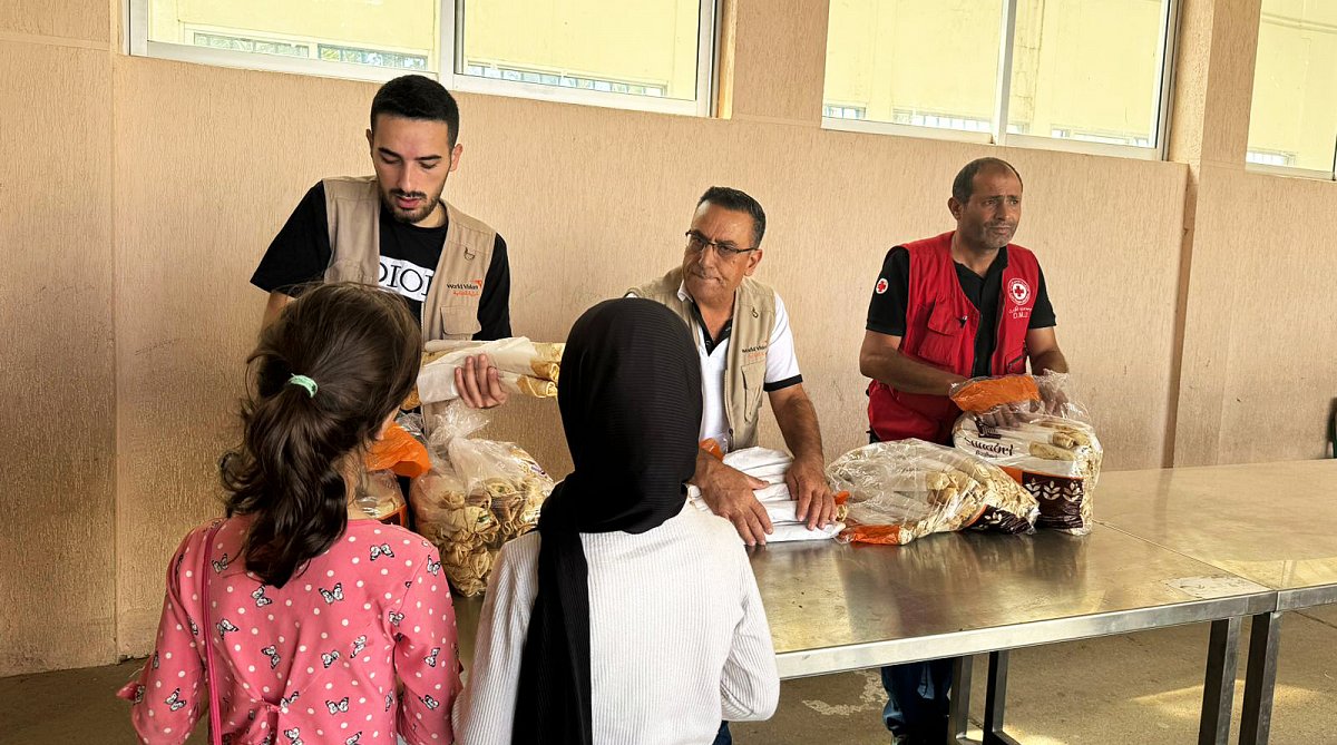 World Vision Mitarbeitende verteilen Lebensmittel, zwei Kinder holen Brotpakete ab.