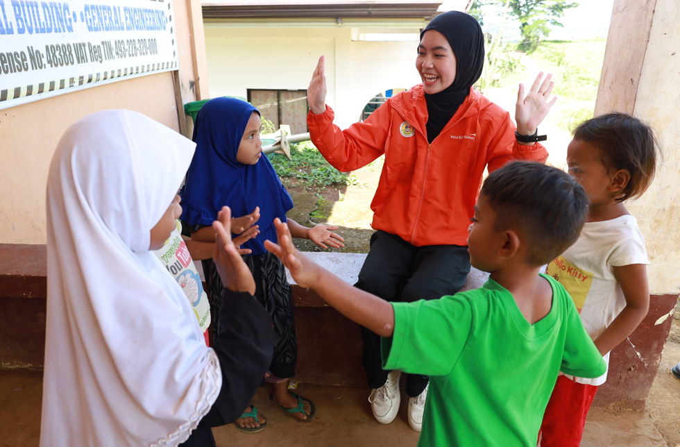 Eine Jugendliche in oranger Jacke kümmert sich um Kinder in den Philippinen.